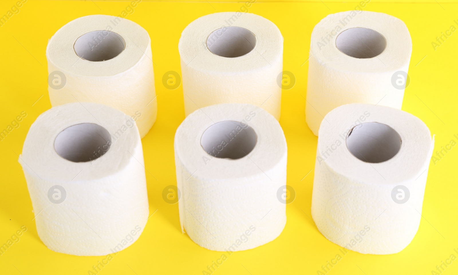 Photo of Many soft toilet paper rolls on yellow background, closeup