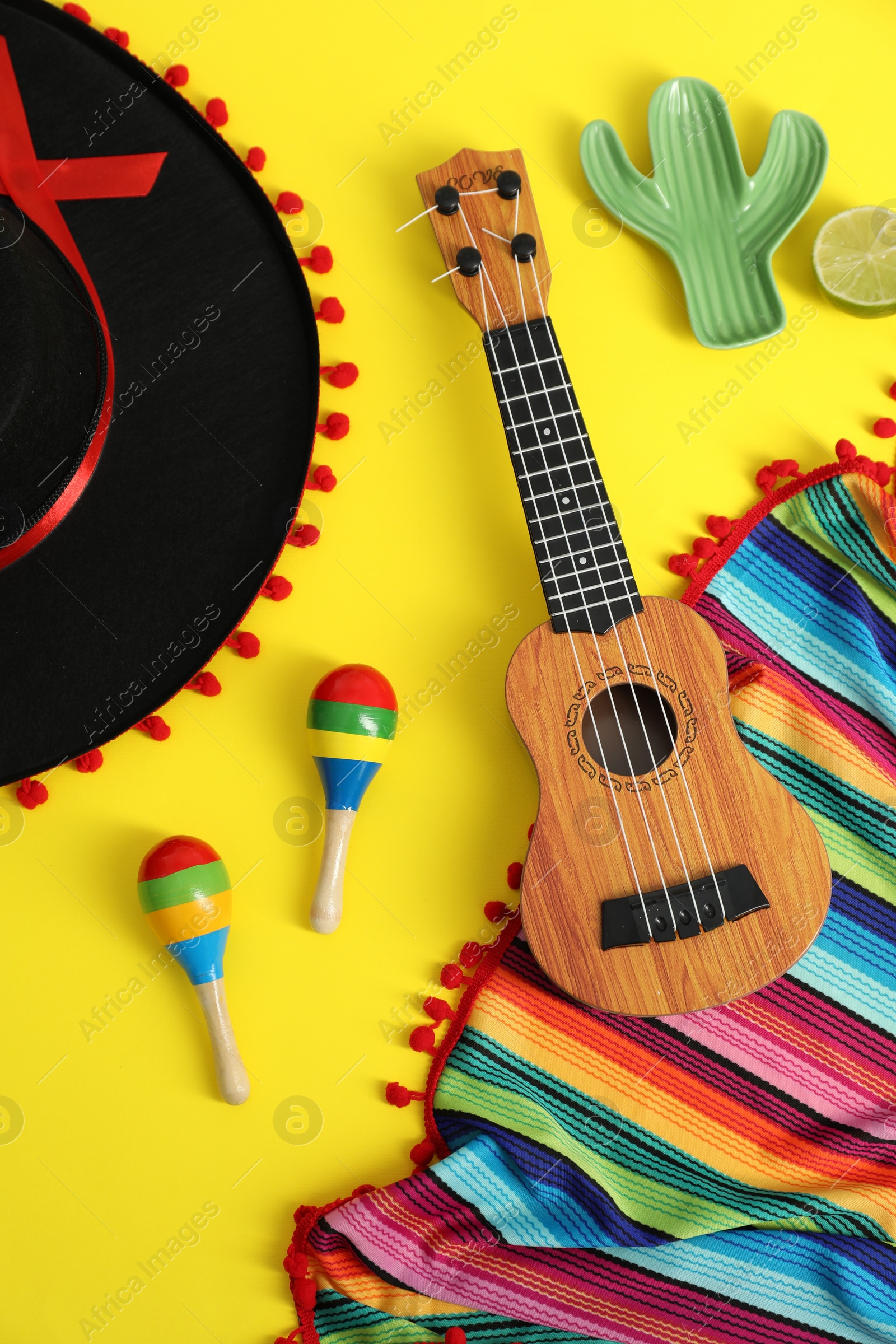 Photo of Flat lay composition with black Flamenco hat, poncho, ukulele and maracas on yellow table