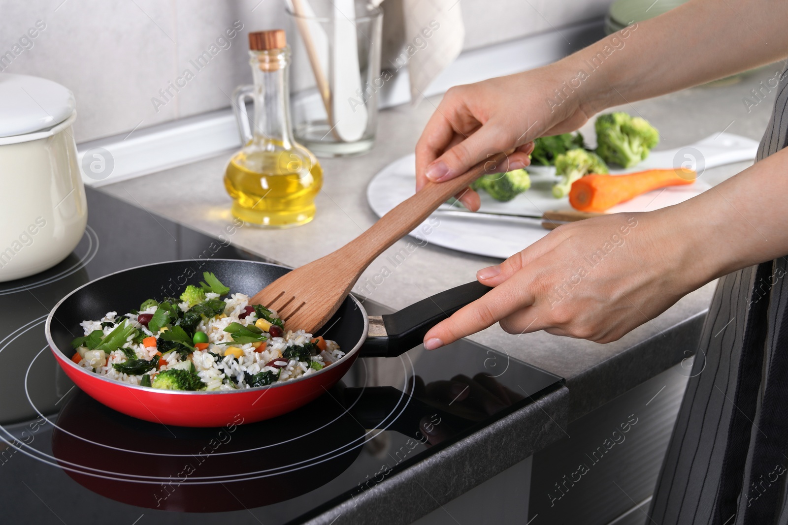 Photo of Woman frying rice with vegetables at induction stove in kitchen, closeup