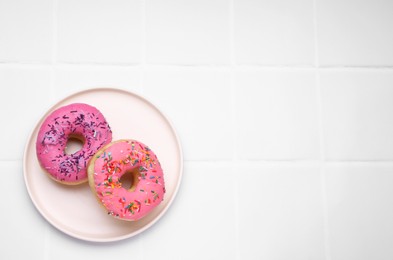 Photo of Glazed donuts decorated with sprinkles on white tiled table, top view. Space for text. Tasty confectionery