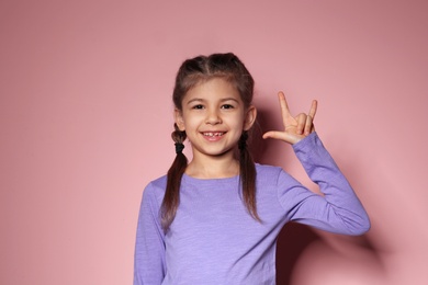 Photo of Little girl showing I LOVE YOU gesture in sign language on color background