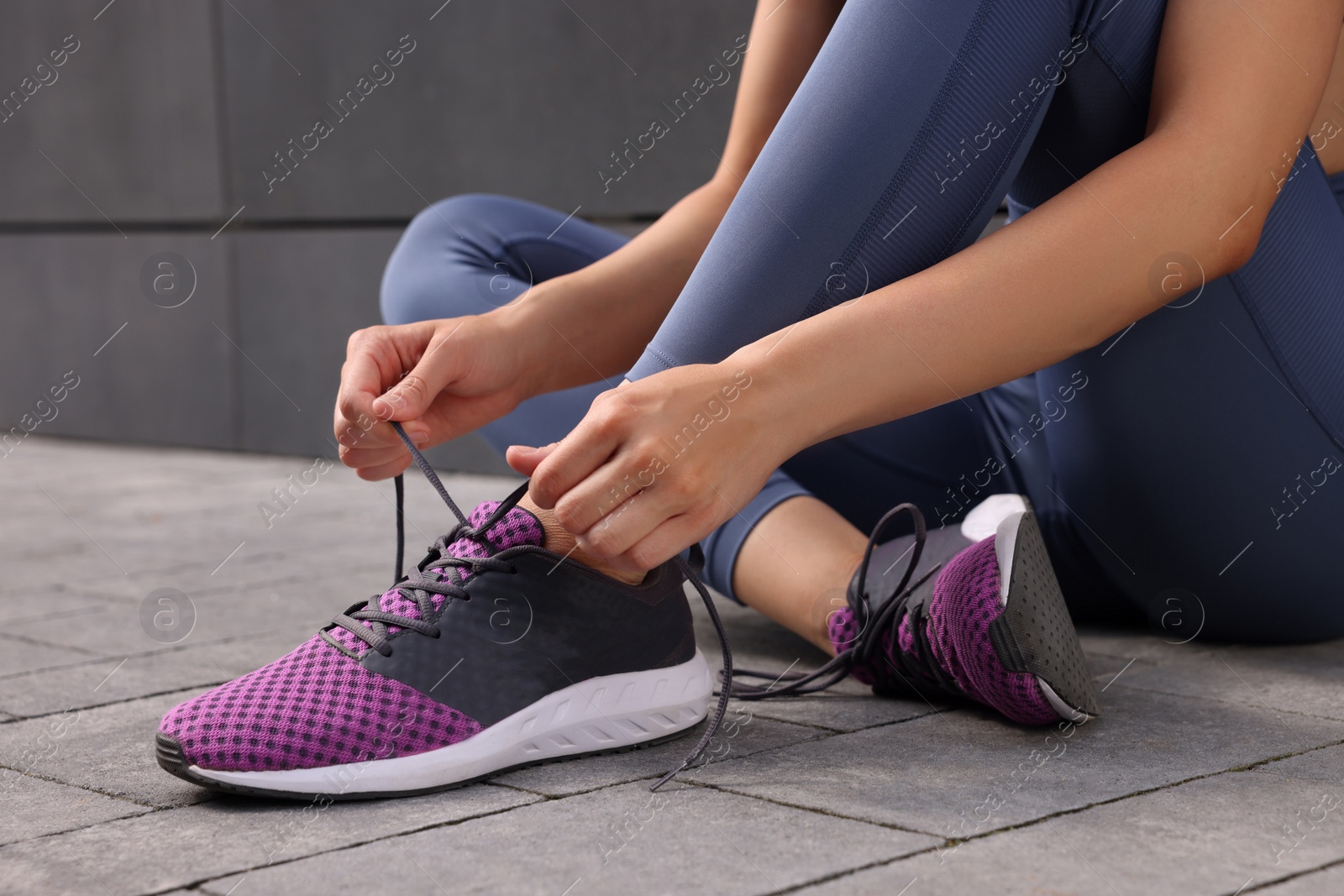 Photo of Woman tying shoelace of sneakers on street, closeup