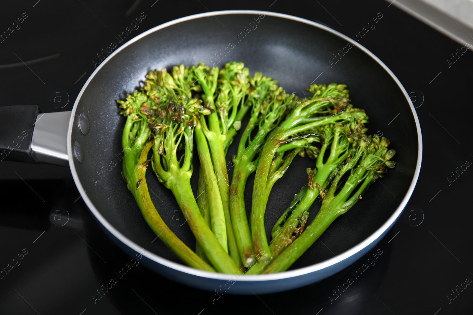 Photo of Frying pan with tasty cooked broccolini on cooktop, closeup