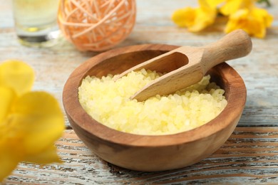 Yellow sea salt in bowl, scoop and flower on wooden table, closeup