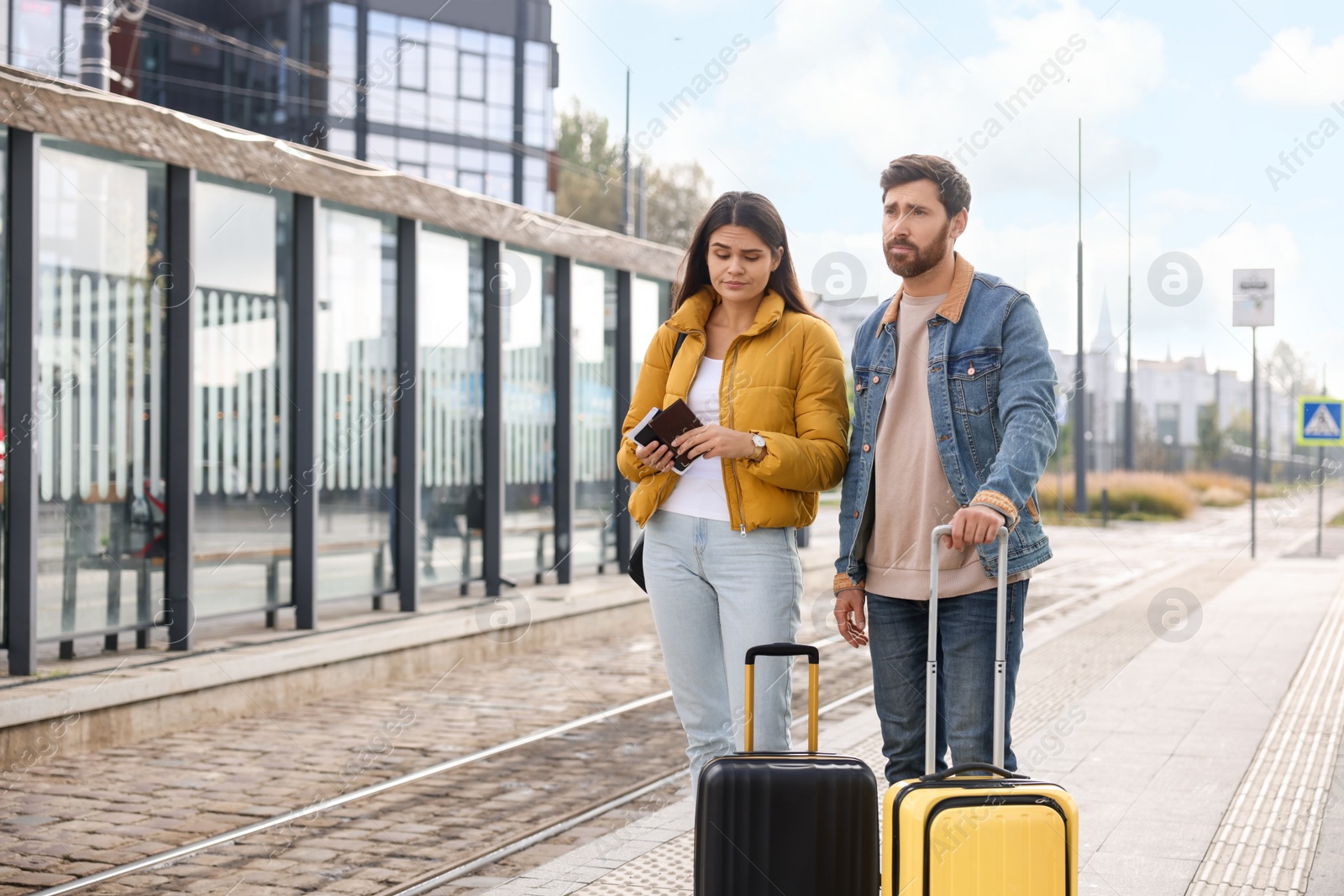 Photo of Being late. Worried couple with suitcases waiting at tram station outdoors, space for text