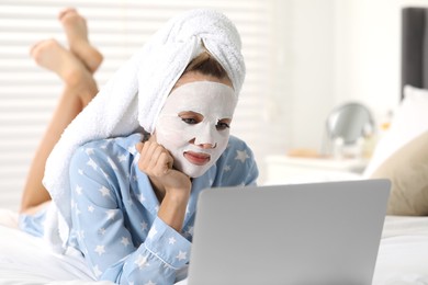 Photo of Young woman with face mask using laptop on bed at home. Spa treatments