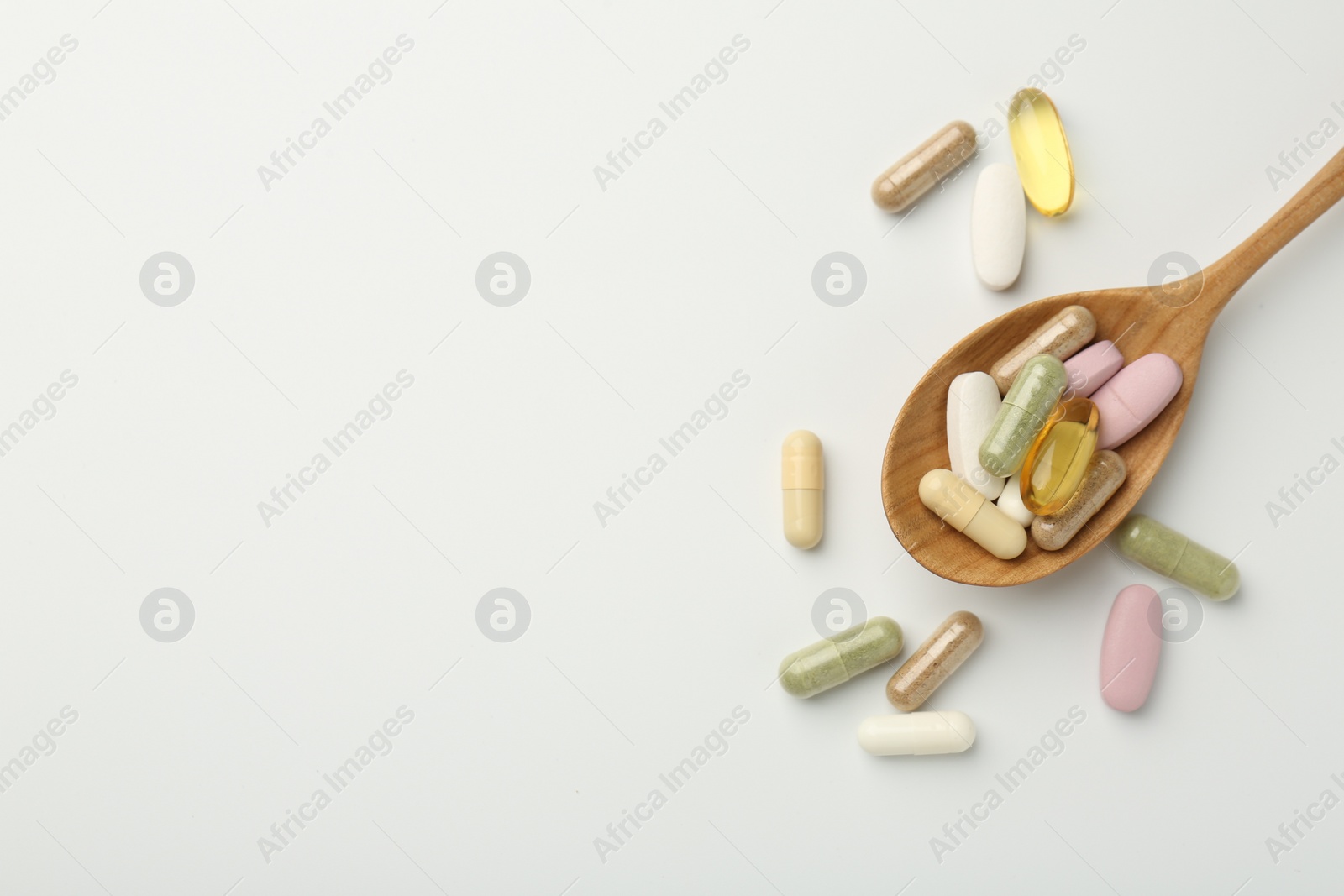 Photo of Different vitamin capsules in spoon on white background, top view. Space for text