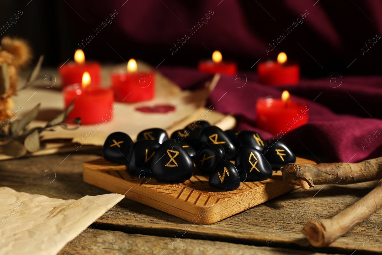 Photo of Many black rune stones and burning candles on wooden table, closeup