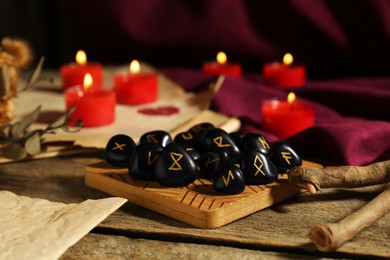Photo of Many black rune stones and burning candles on wooden table, closeup