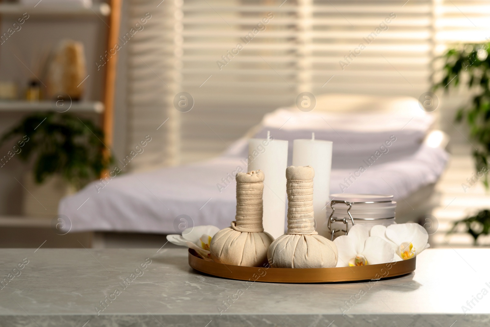 Photo of Tray with herbal bags, candles, scrub and beautiful flowers on grey marble table in salon, space for text. Spa products