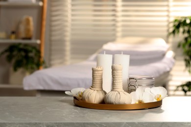 Photo of Tray with herbal bags, candles, scrub and beautiful flowers on grey marble table in salon, space for text. Spa products