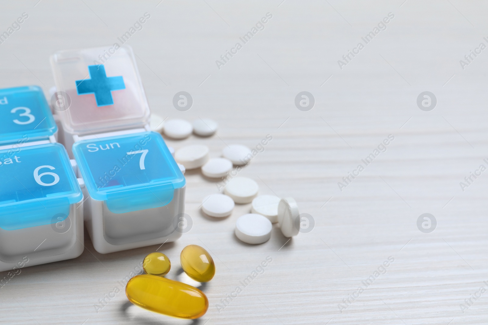 Photo of Weekly pill box with medicaments on white wooden table, closeup. Space for text