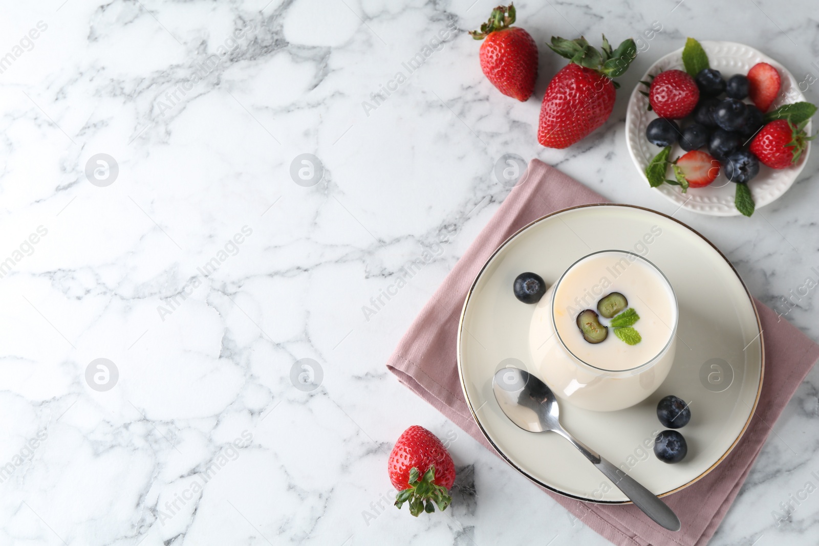 Photo of Tasty yogurt in glass and berries on white marble table, flat lay. Space for text