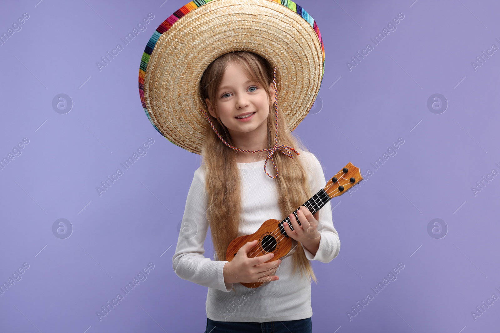 Photo of Cute girl in Mexican sombrero hat playing ukulele on purple background