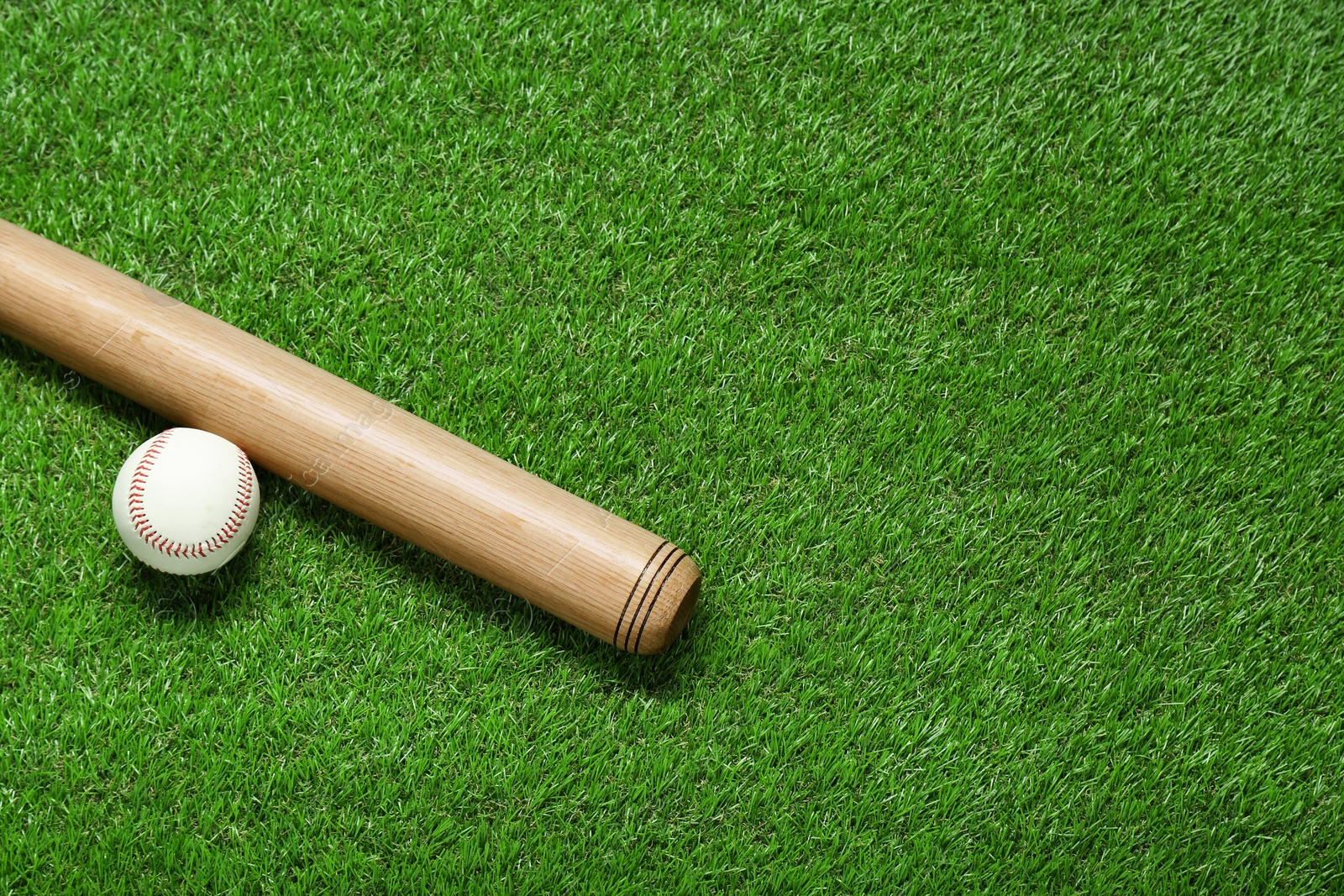 Photo of Wooden baseball bat and ball on green grass, flat lay. Space for text