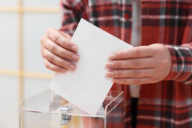 Photo of Woman putting her vote into ballot box on blurred background, closeup