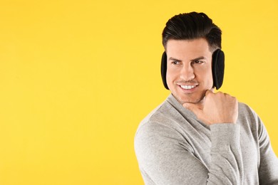 Photo of Man wearing stylish earmuffs on yellow background. Space for text