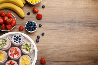 Photo of Yogurt maker with jars and different fruits on wooden table, flat lay. Space for text