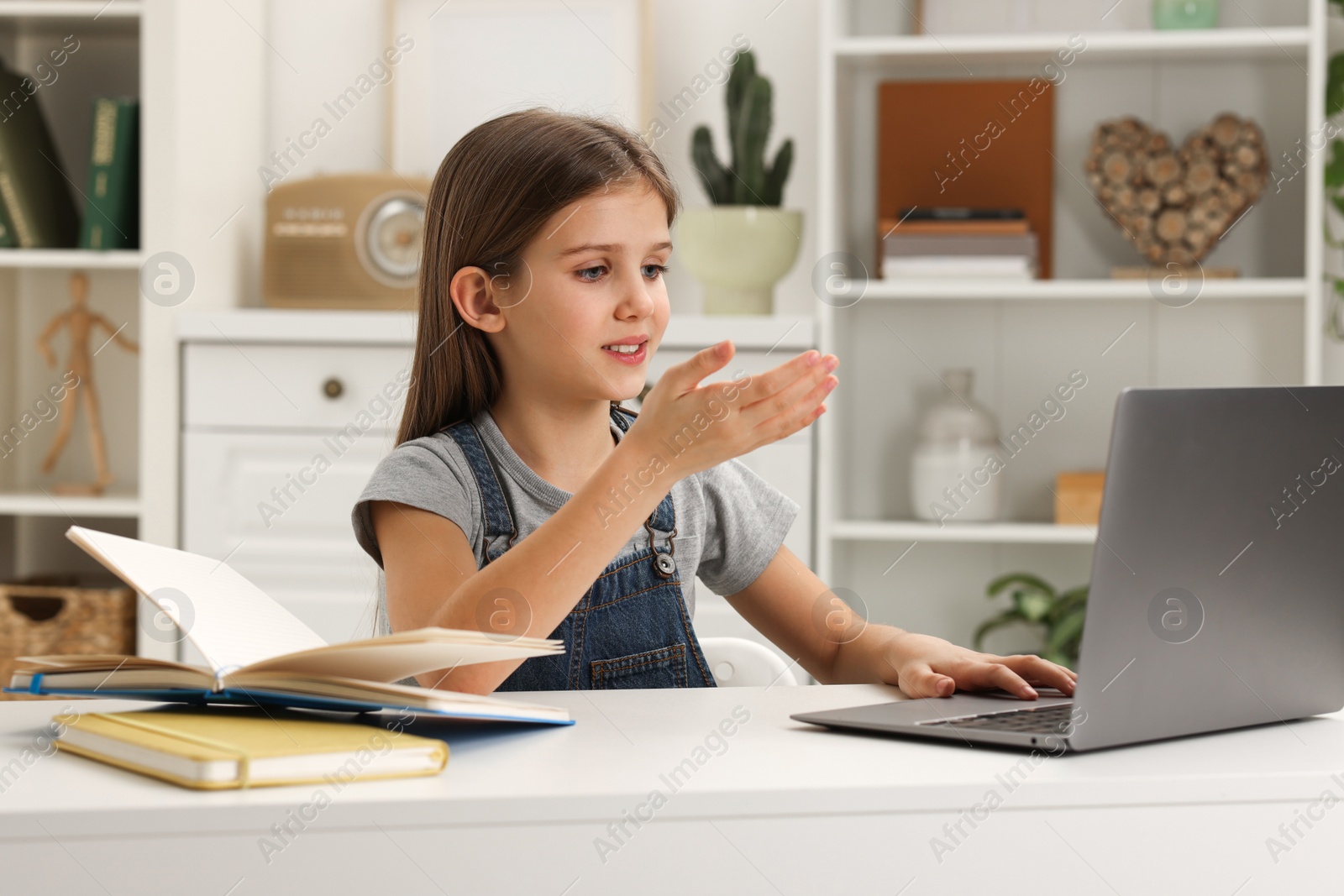 Photo of Cute girl using laptop at white table indoors