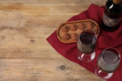 Photo of Red wine and chocolate truffles on wooden table, above view. Space for text
