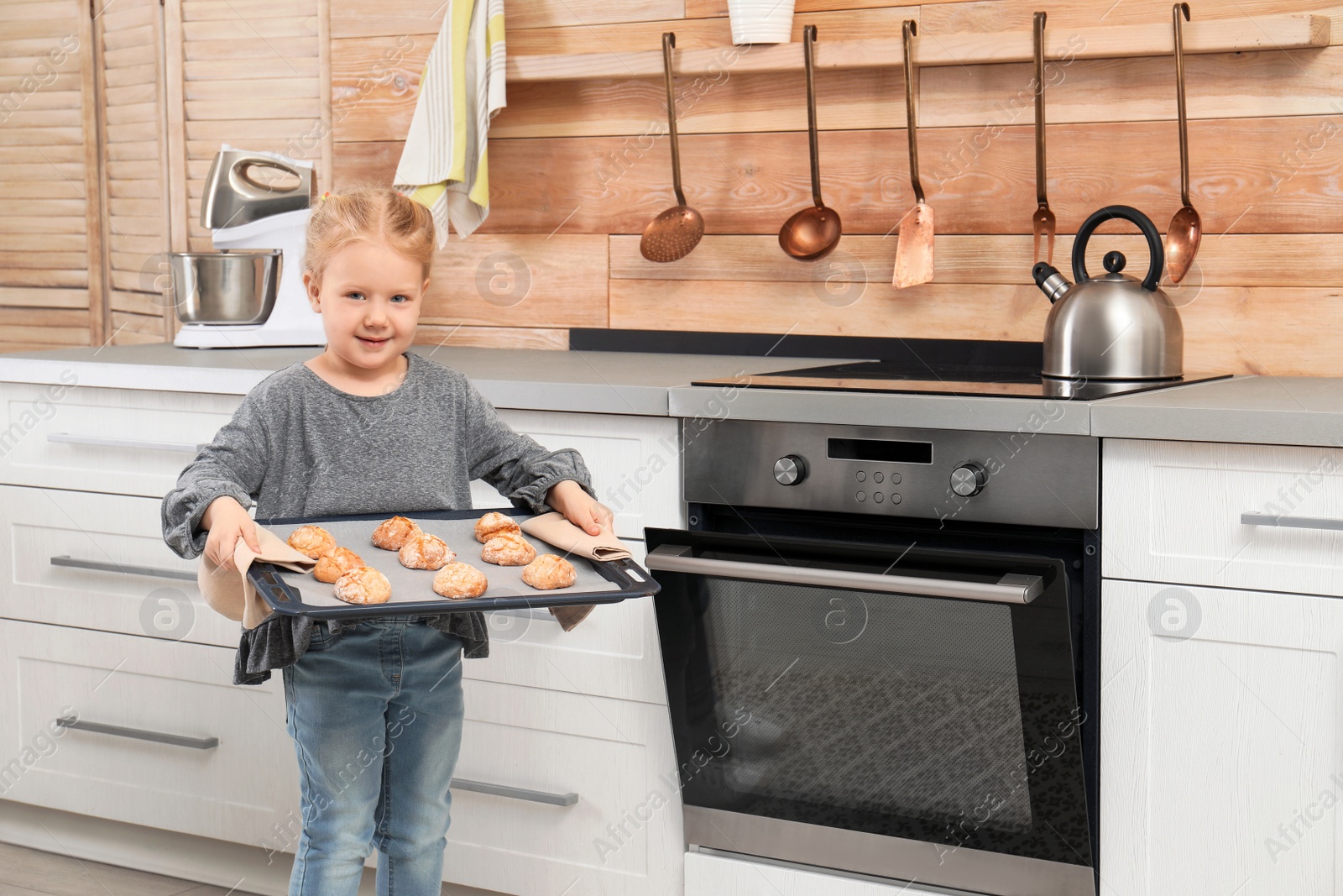 Photo of Cute little girl with sheet pan of oven baked cookies in kitchen