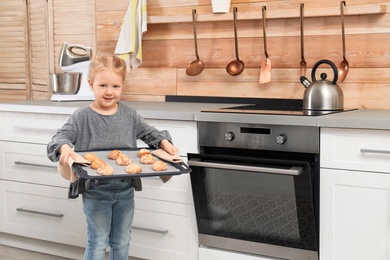 Cute little girl with sheet pan of oven baked cookies in kitchen