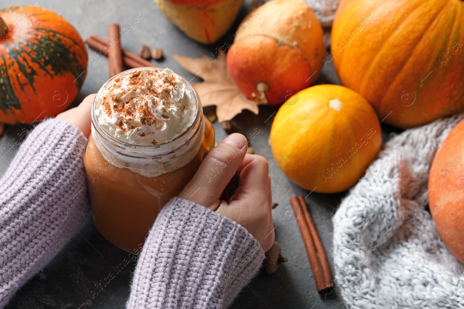 Photo of Woman holding mason jar of tasty pumpkin spice latte on gray table, closeup