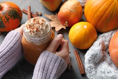 Woman holding mason jar of tasty pumpkin spice latte on gray table, closeup