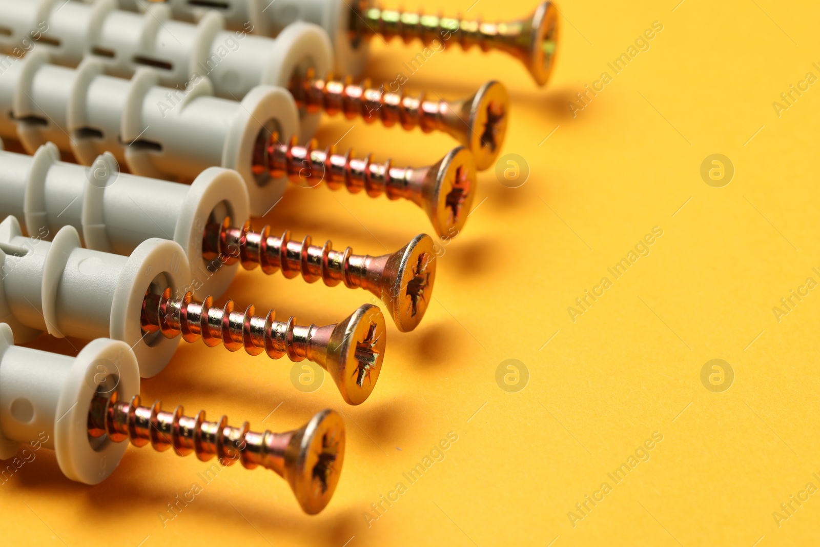 Photo of Many metal screws with dowels on orange background, closeup. Space for text