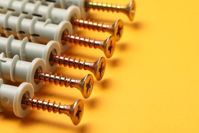 Photo of Many metal screws with dowels on orange background, closeup. Space for text