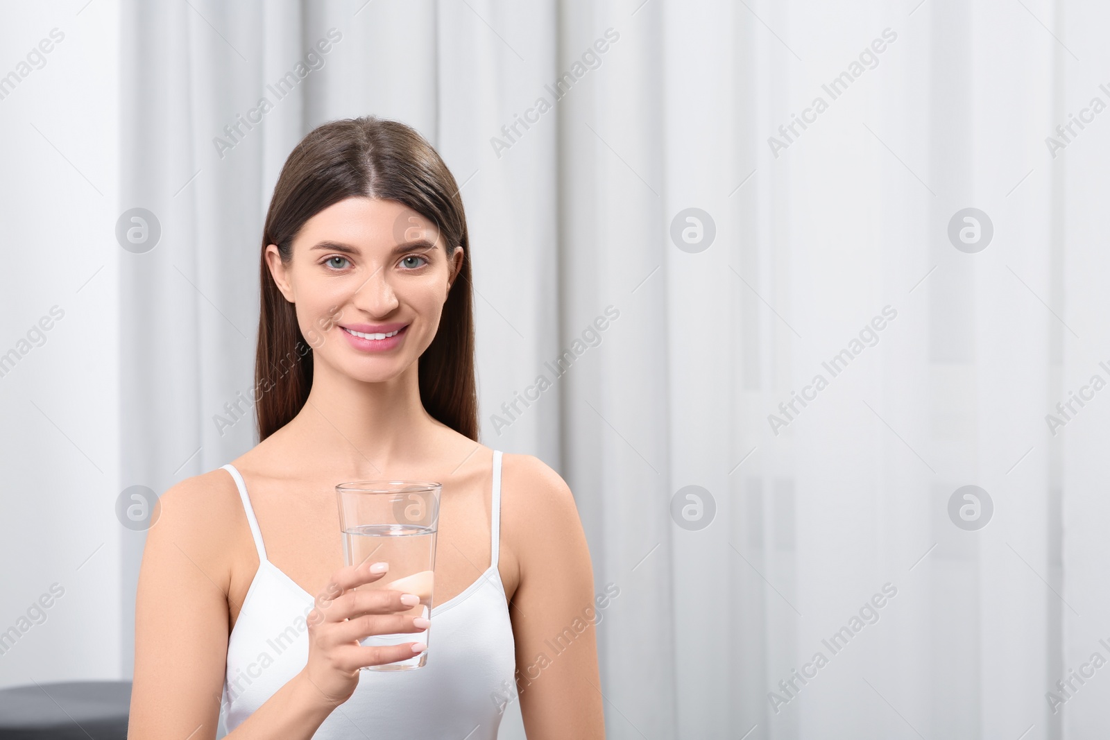 Photo of Healthy habit. Portrait of smiling woman holding glass with fresh water indoors. Space for text