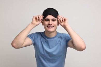 Happy man in pyjama and sleep mask on light grey background