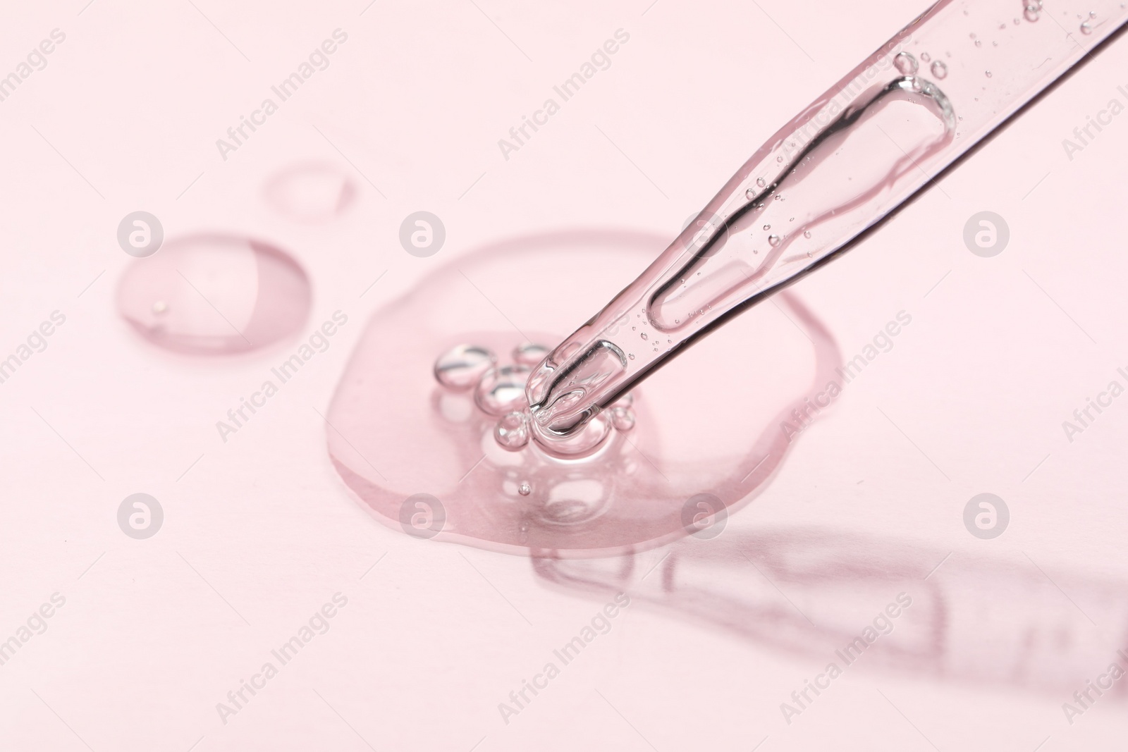 Photo of Glass pipette and transparent liquid on light pink background, closeup