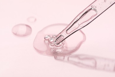 Glass pipette and transparent liquid on light pink background, closeup