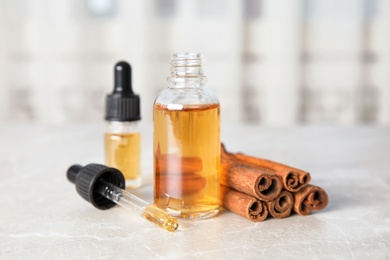 Photo of Bottles of essential oils and cinnamon sticks on grey marble table