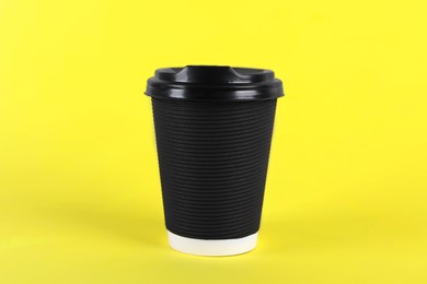 Black paper cup with plastic lid on yellow background. Coffee to go