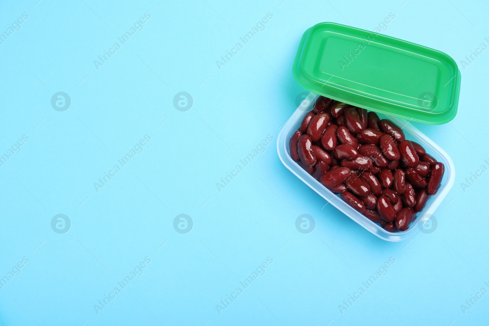 Photo of Fresh red kidney beans in glass container on light blue background, top view. Space for text