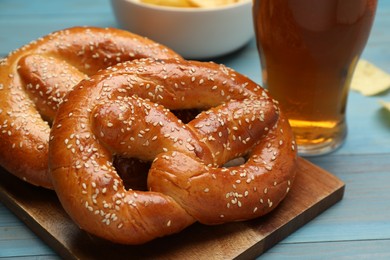 Tasty freshly baked pretzels and glass of beer on light blue wooden table, closeup