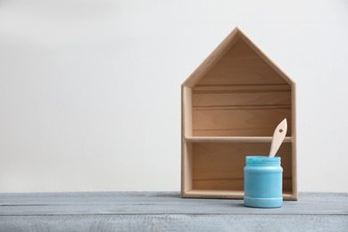 Photo of Brush with paint and wooden house model on grey table. Space for text