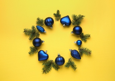 Photo of Beautiful festive wreath made of blue Christmas balls and fir tree branches on yellow background, top view
