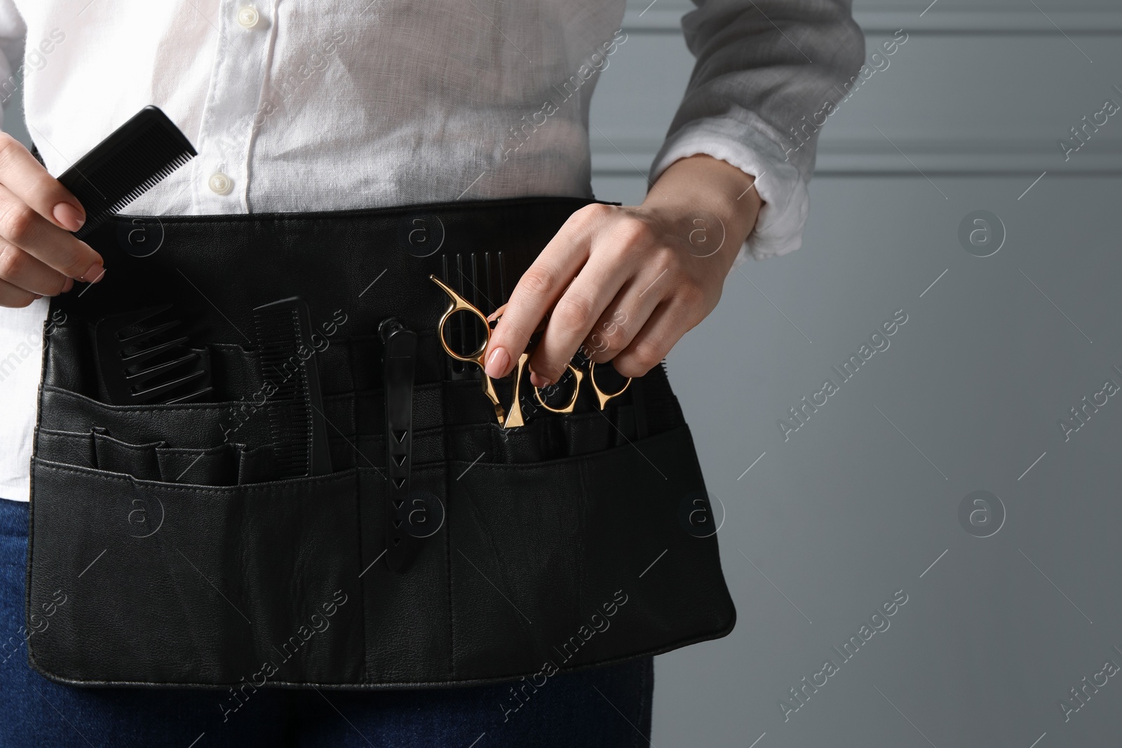 Photo of Hairstylist with professional tools in waist pouch near grey wall, closeup. Space for text