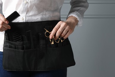 Photo of Hairstylist with professional tools in waist pouch near grey wall, closeup. Space for text