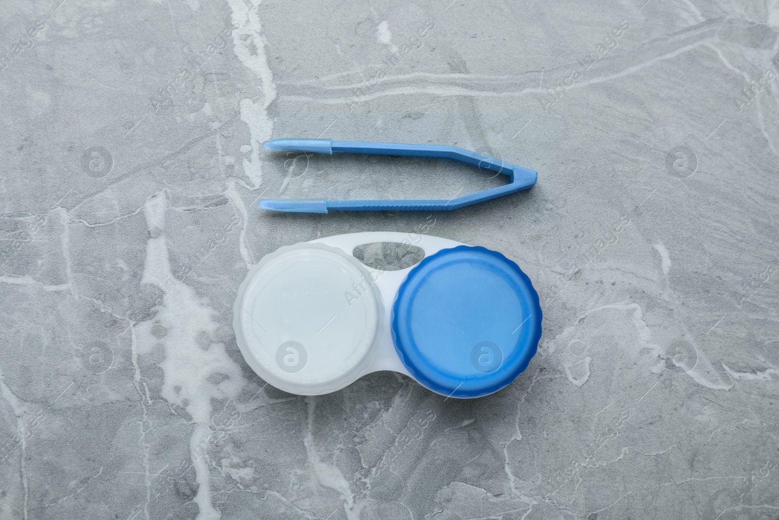 Photo of Case with contact lenses and tweezers on light grey marble table, flat lay