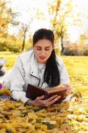 Woman reading book in park on autumn day