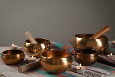 Photo of Tibetan singing bowls with mallets and burning candles on colorful fabric