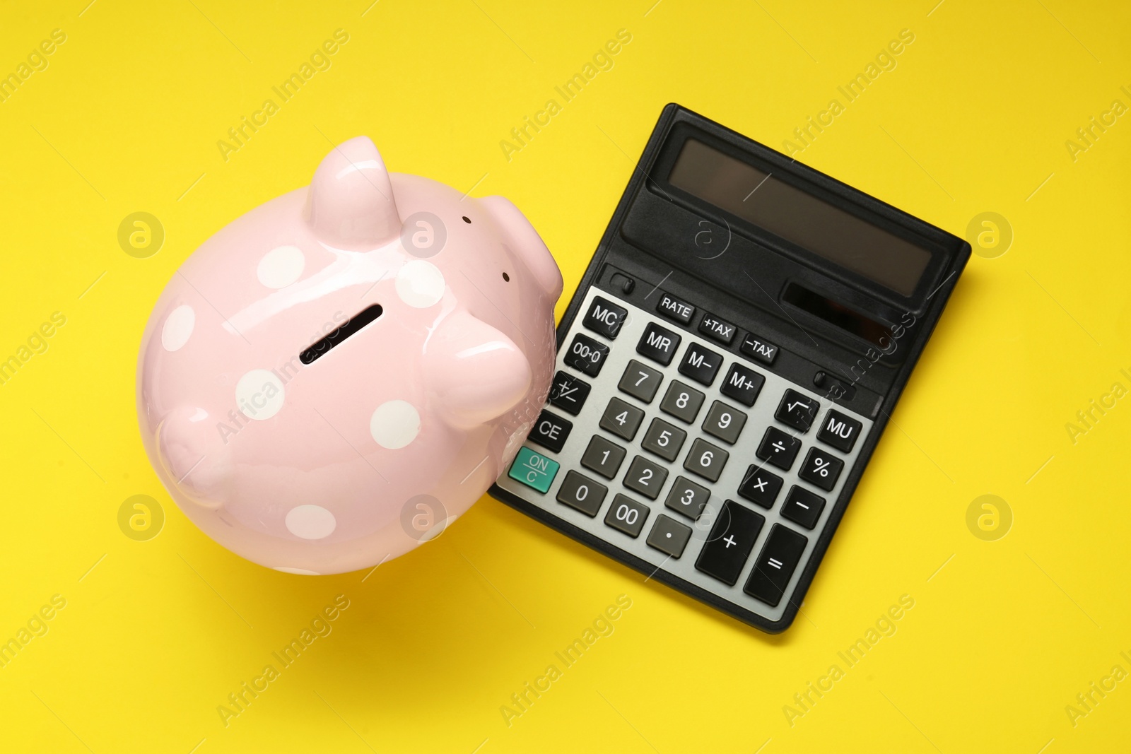 Photo of Calculator and piggy bank on yellow background, top view