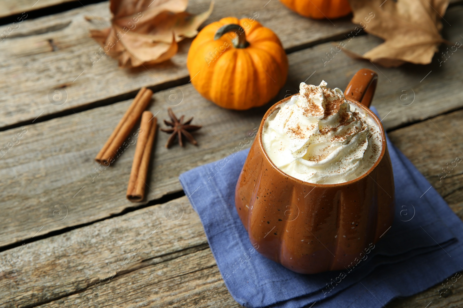 Photo of Mug of pumpkin spice latte with whipped cream and ingredients on wooden table. Space for text