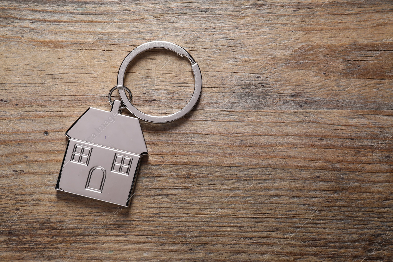 Photo of Metal keychain in shape of house on wooden table, top view. Space for text