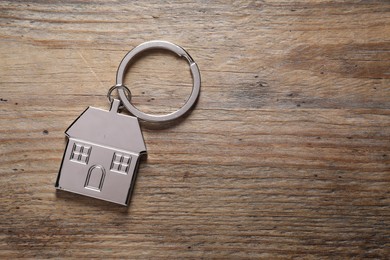 Metal keychain in shape of house on wooden table, top view. Space for text