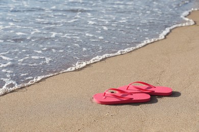 Photo of Stylish bright pink flip flops on sand near sea. Space for text